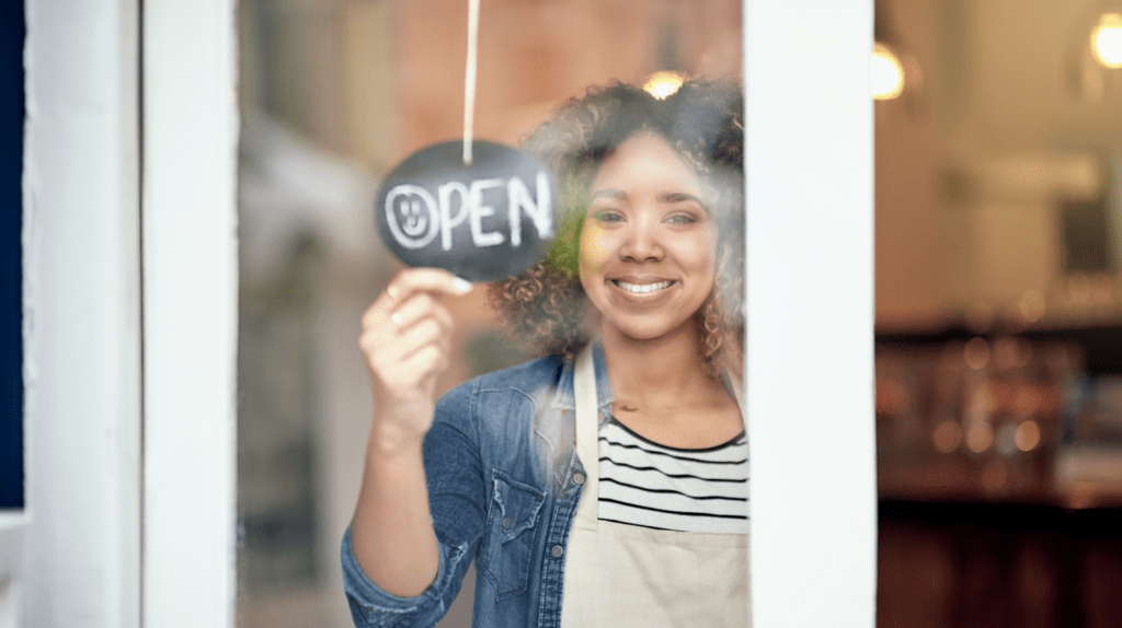Woman business owner flipping sign to "open" Common Business Mistakes New Business Owners Make